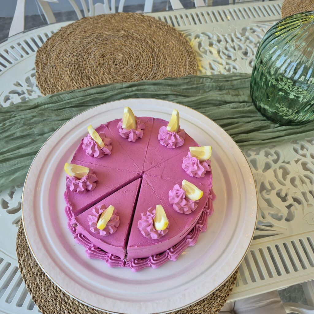 A vibrant pink frosted cake adorned with lemon slices on a decorative white table.